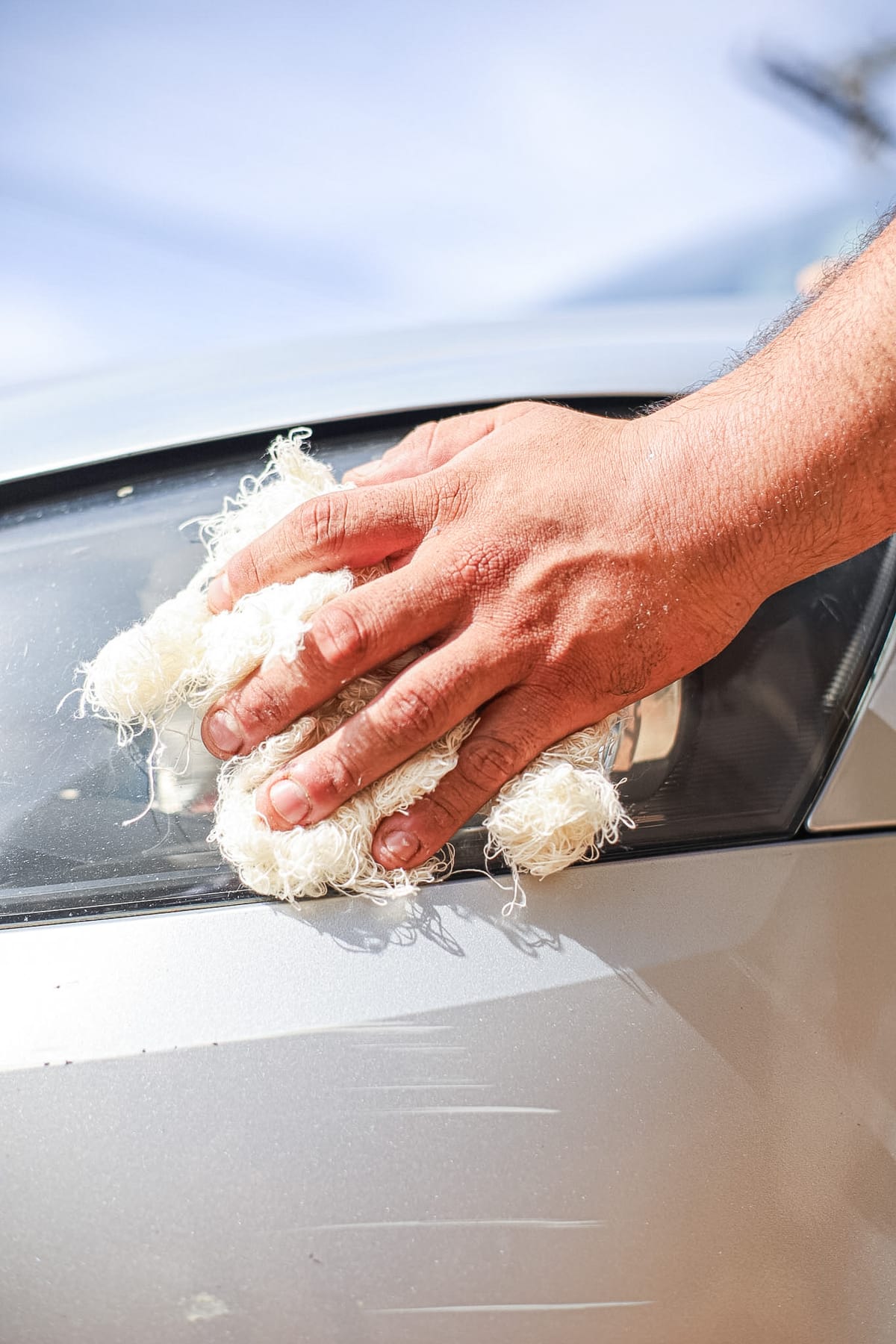 Mão usando estopa branca Bril para limpar carro